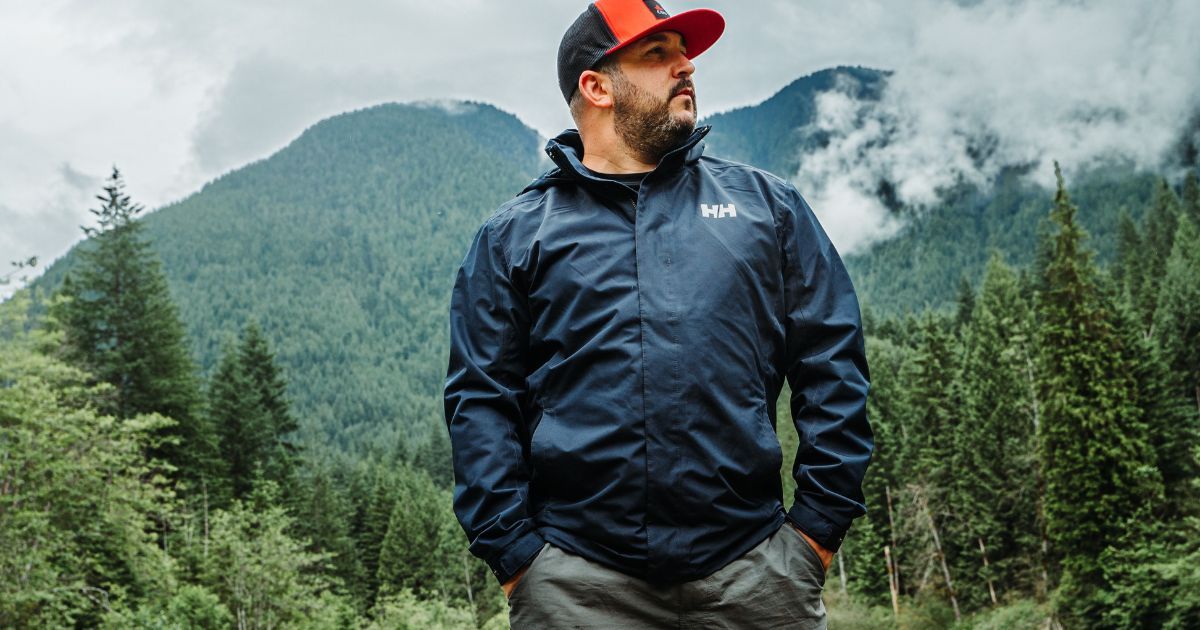 man in rain jacket with trees and mountains in the background