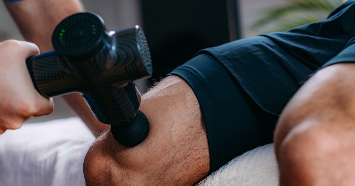 man using a massage gun on quads