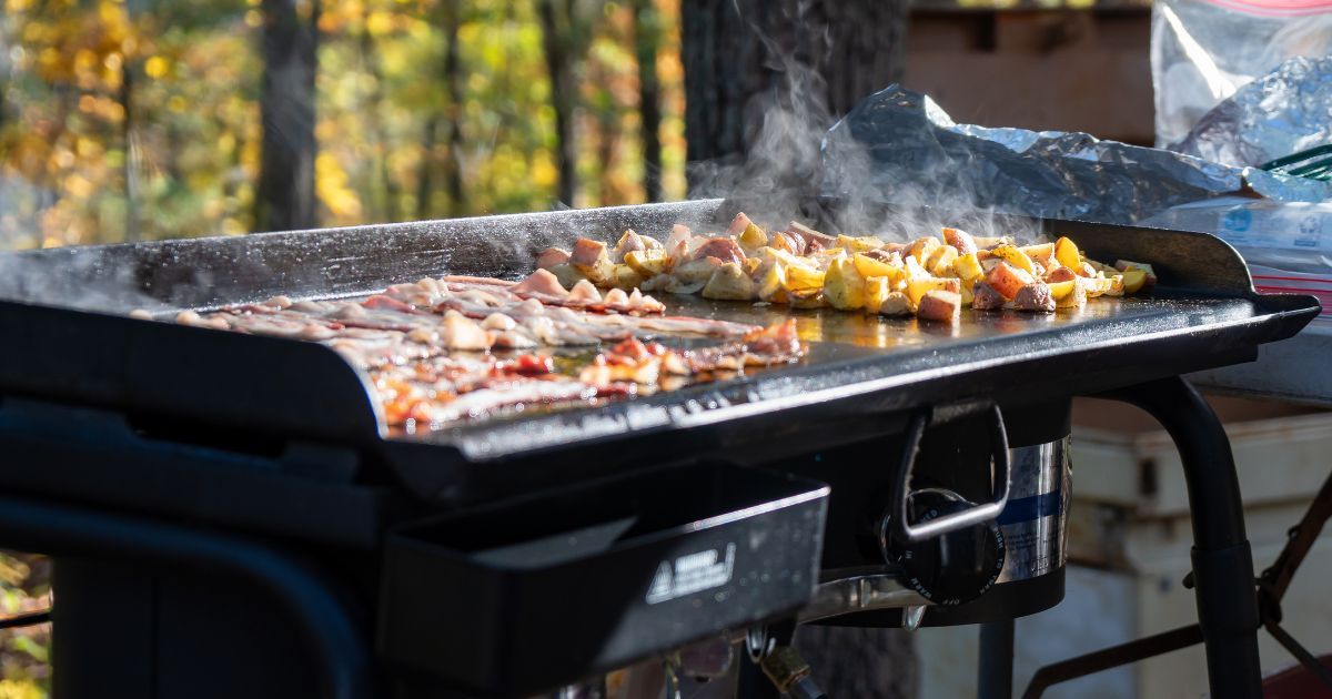 camping griddle with bacon and potatoes on it