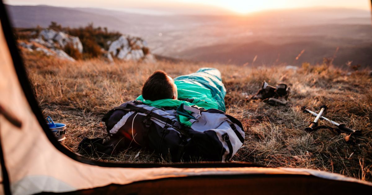 man lying in sleeping bag watching the sunset