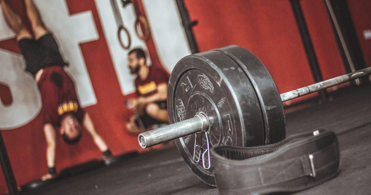 barbell in focus and man doing handstand pushups in background