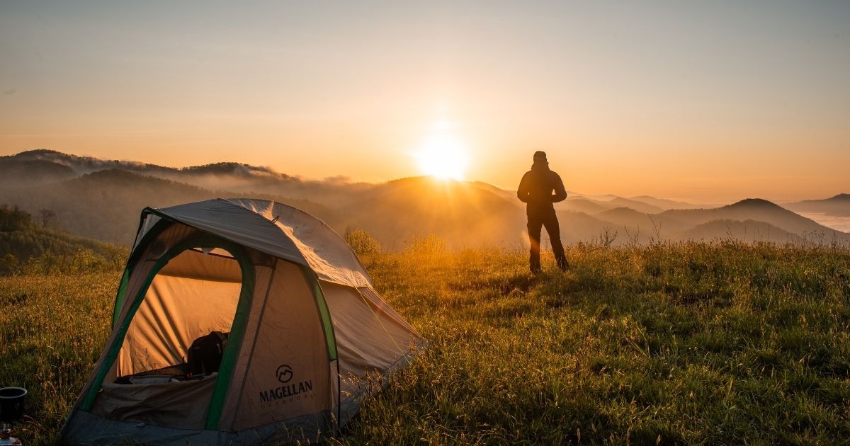 tent in foreground, while a person watches sunset