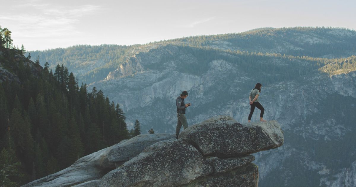 two people standing on rock overlooking mountains